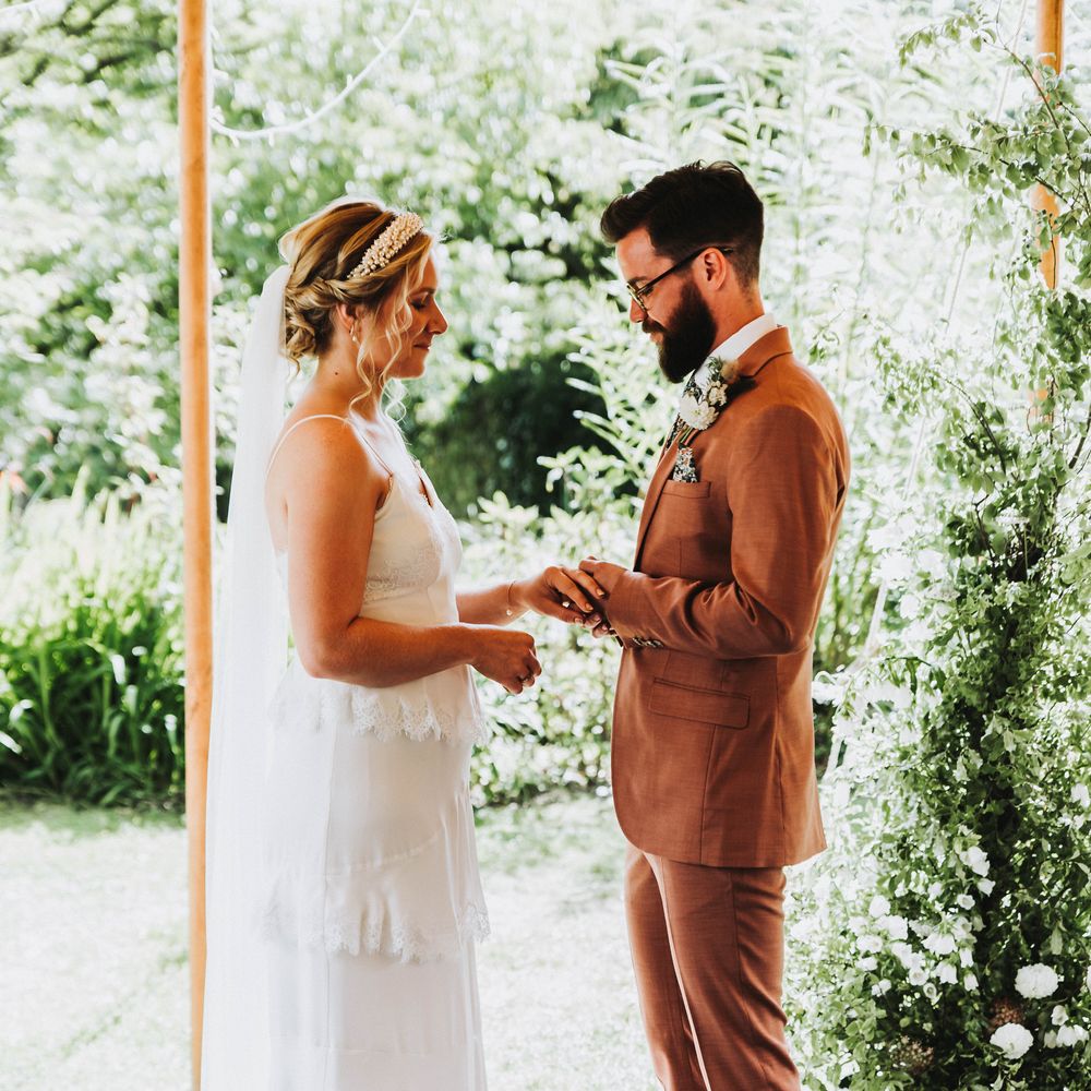 Bride & groom hold hands during wedding ceremony on a bright and sunny day outdoors in Cornwall