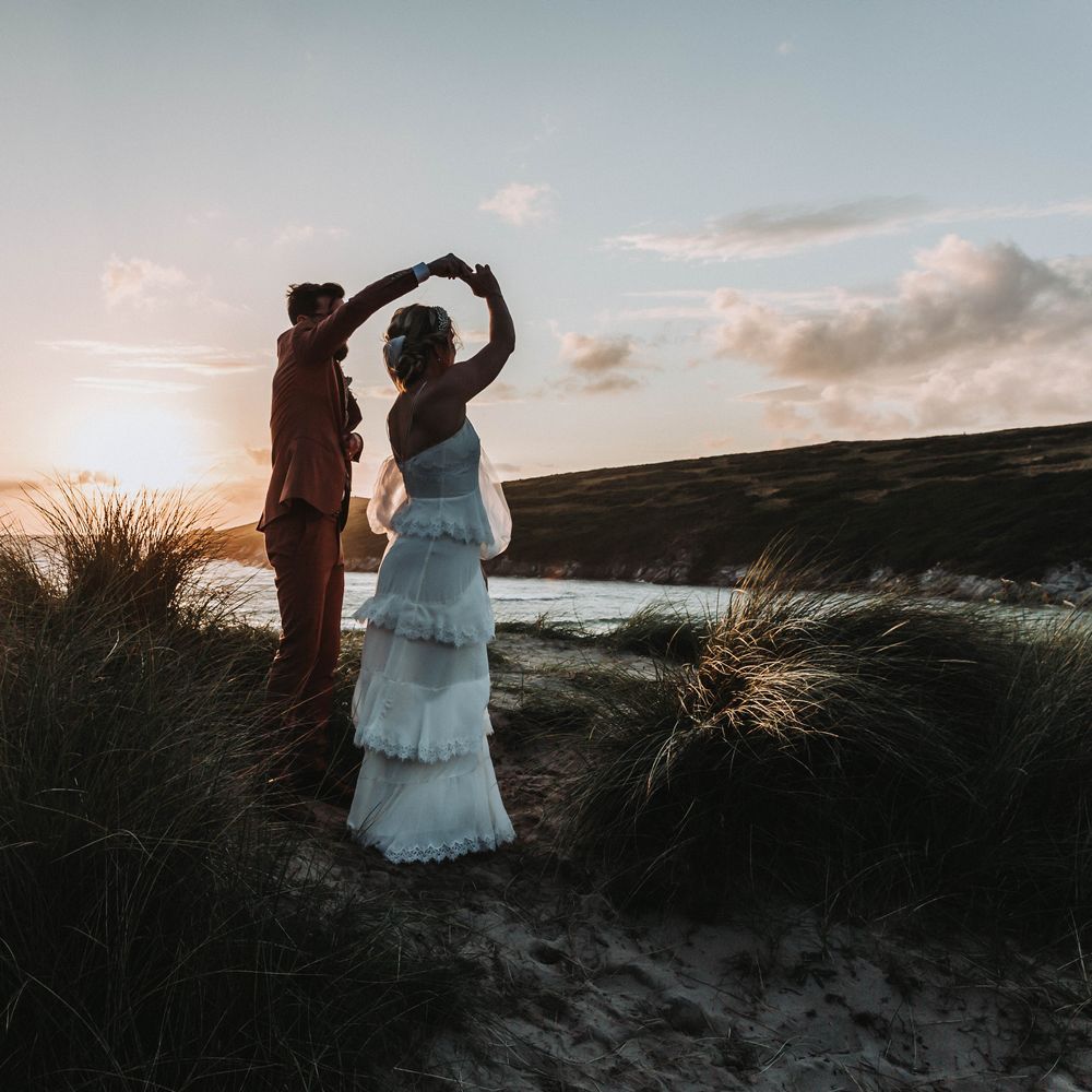 Groom spins his bride around on the beach on their wedding day as the sun goes down