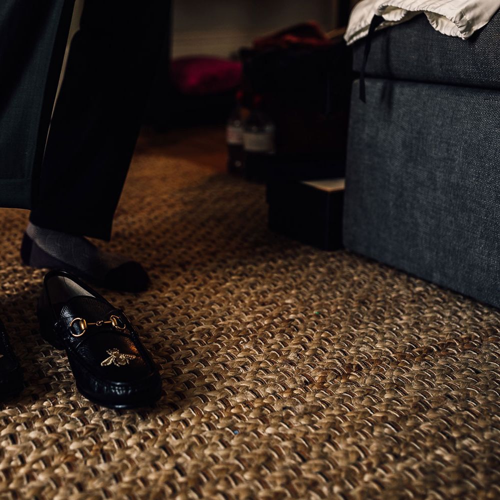 Groom in black and white patterned socks puts on leather loafers before Cornish wedding 