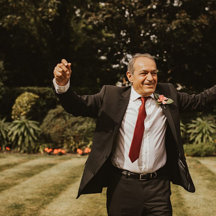 Father of the Bride celebrates as he walks across on lawn on wedding day