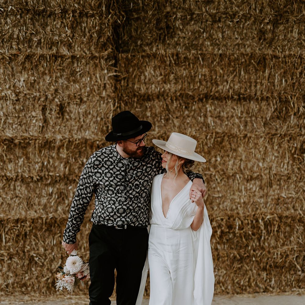 Bride & groom hug one another closely on the day of their wedding in front of hay bales 