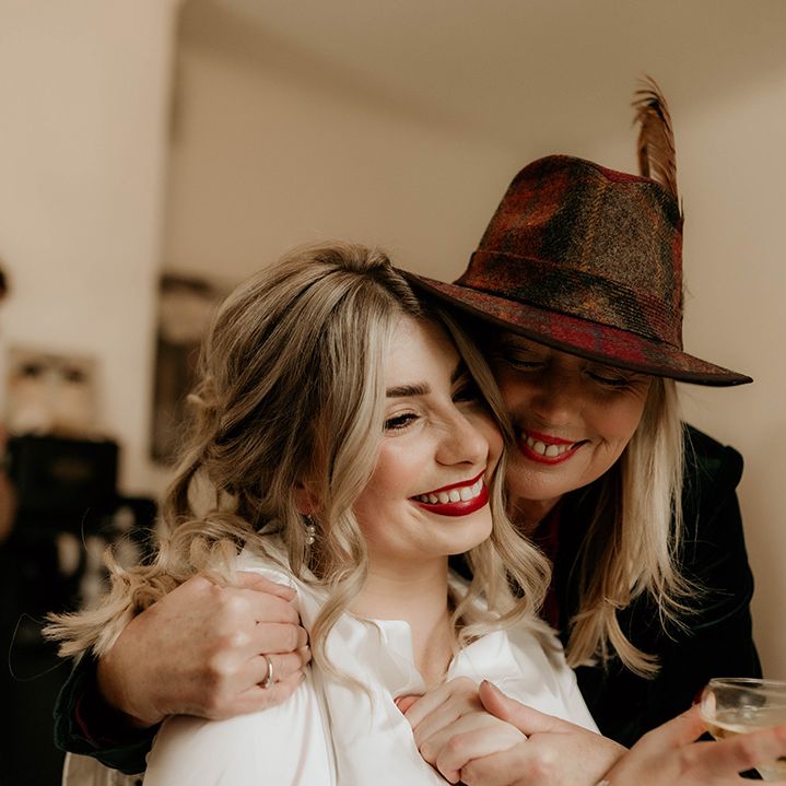 Wedding guest in a felt fedora embracing the bride on the wedding morning 