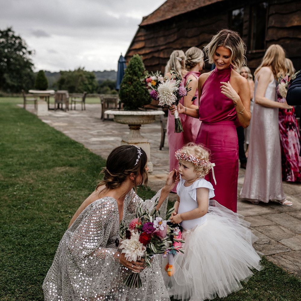 Bride in a silver wedding dress talking to her little flower girl in a tulle skirt 