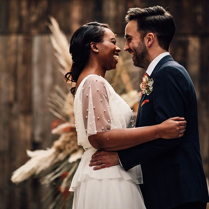 Groom in a navy suit embracing his bride in a sheer sleeve wedding dress at their 100 Barrington wedding ceremony 
