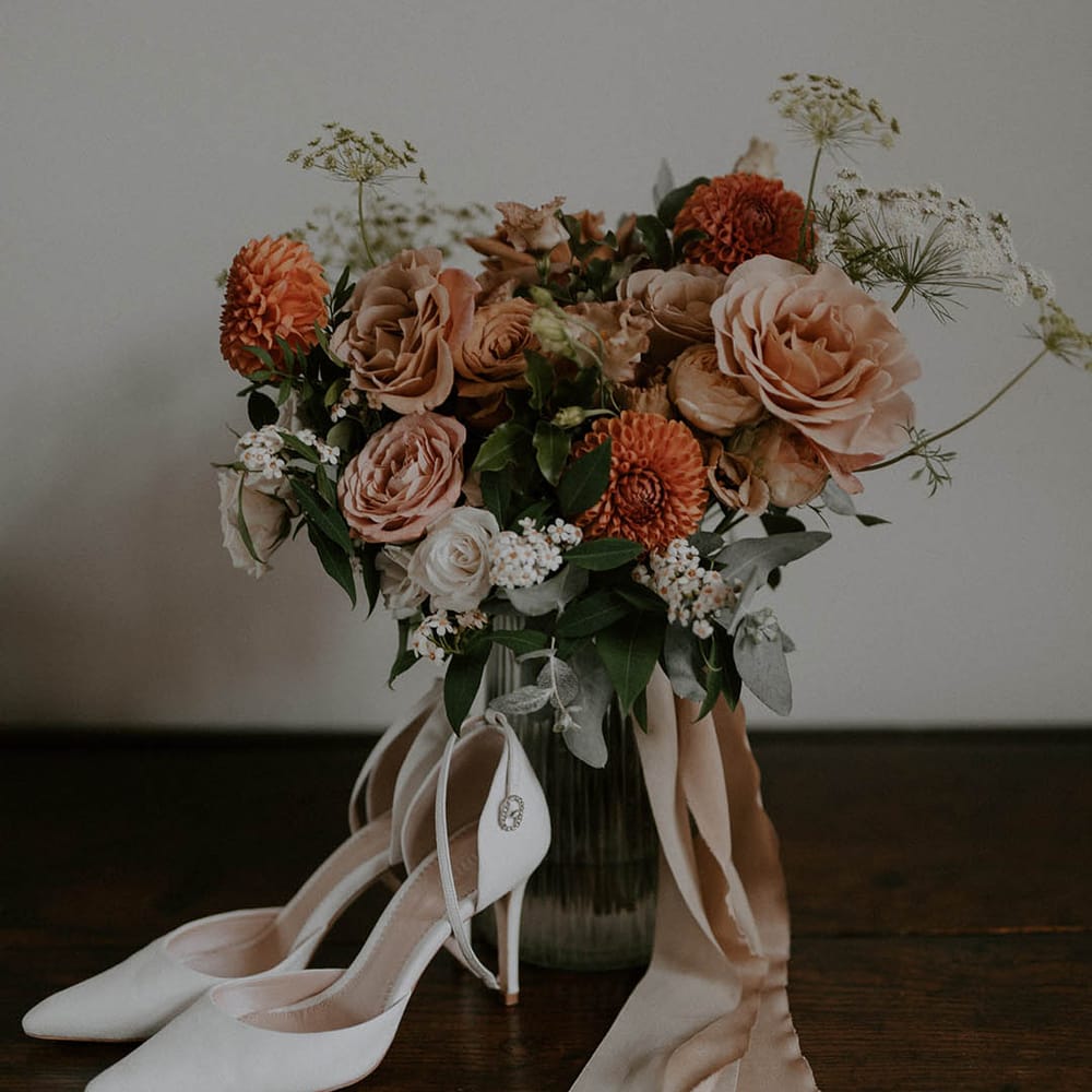White wedding shoes with orange and blush wedding bouquet tied with pink ribbon
