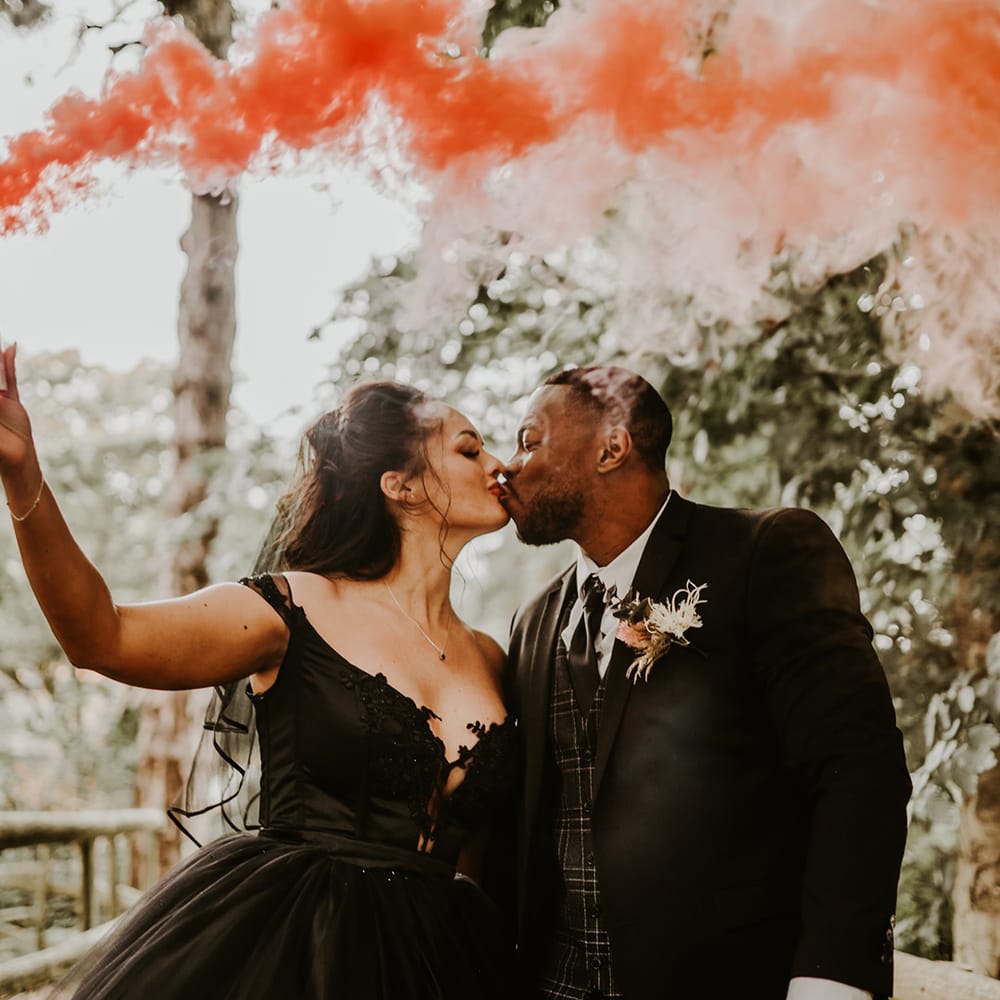 Bride holds pink smoke bomb as she kisses her husband 