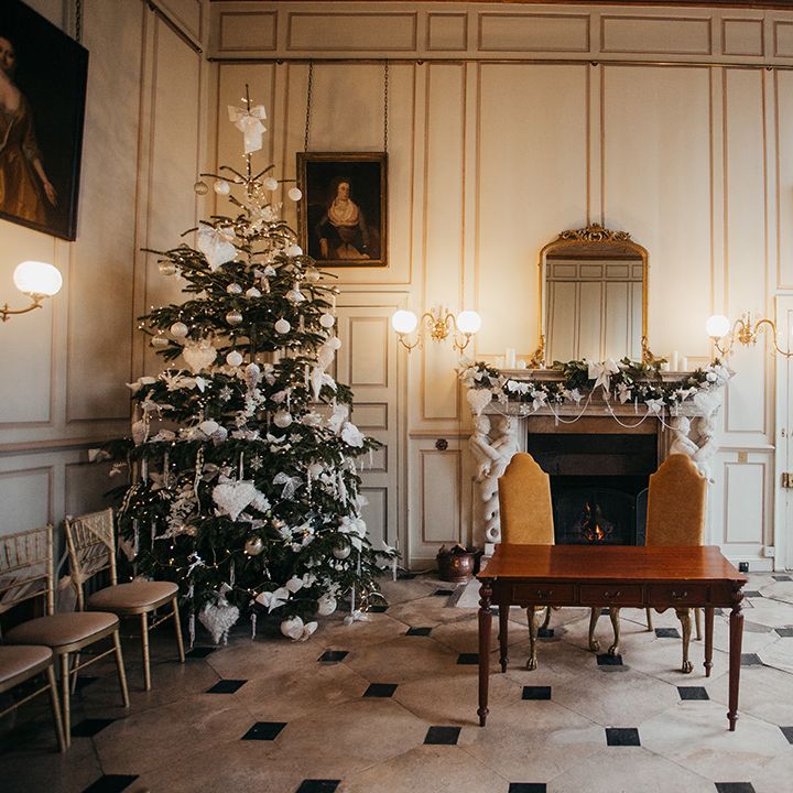 Christmas tree sits in the corner of grand room at Gosfield Hall complete with wreath across fireplace 