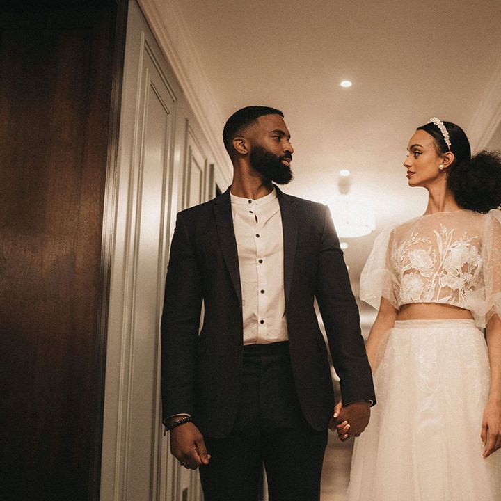 Black groom in an open collar shirt and forest green suit holding hands with his Black bride in lace bridal separates 
