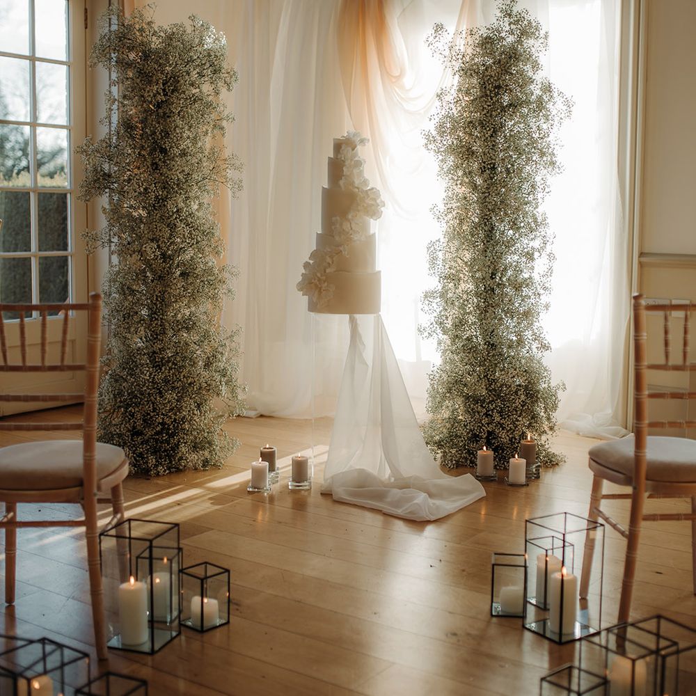 Tall five tier white wedding cake, hanging drapes and gypsophila flower cloud columns at Hodsock Priory 