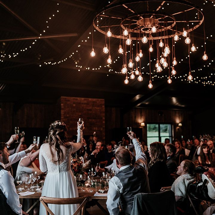 Bride stands and makes a bridal speech as everyone raises a toast in cosy and rustic barn wedding venue at Silchester Farm