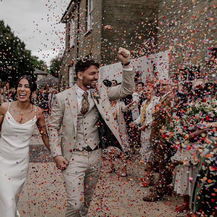 Colourful confetti photograph with bride in a slip wedding dress and groom in a stone three piece suit with paisley tie 