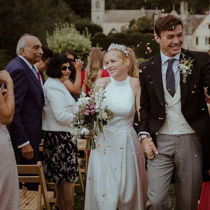 Smiling bride and groom walk back down the aisle through confetti after handfasting ceremony 