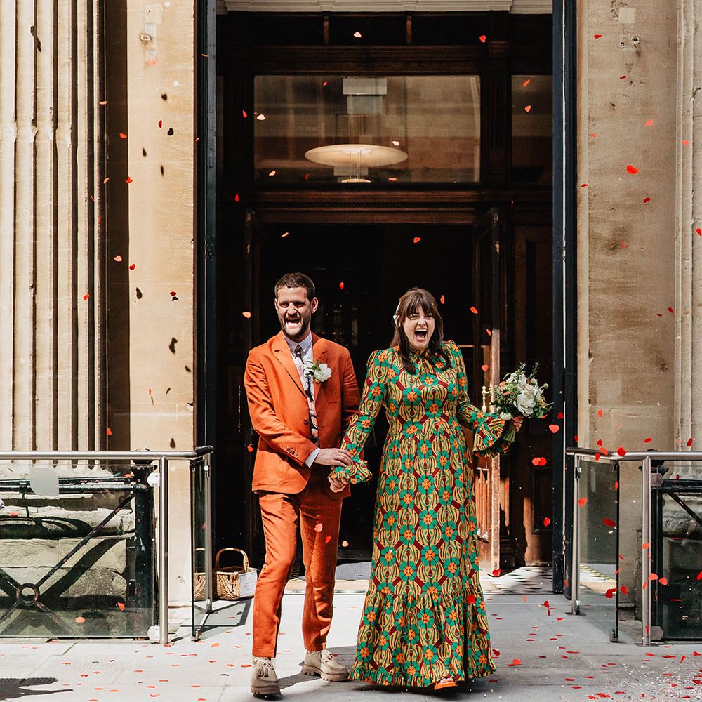 Bride & groom walk through doorway to heart shaped confetti around them outdoors 