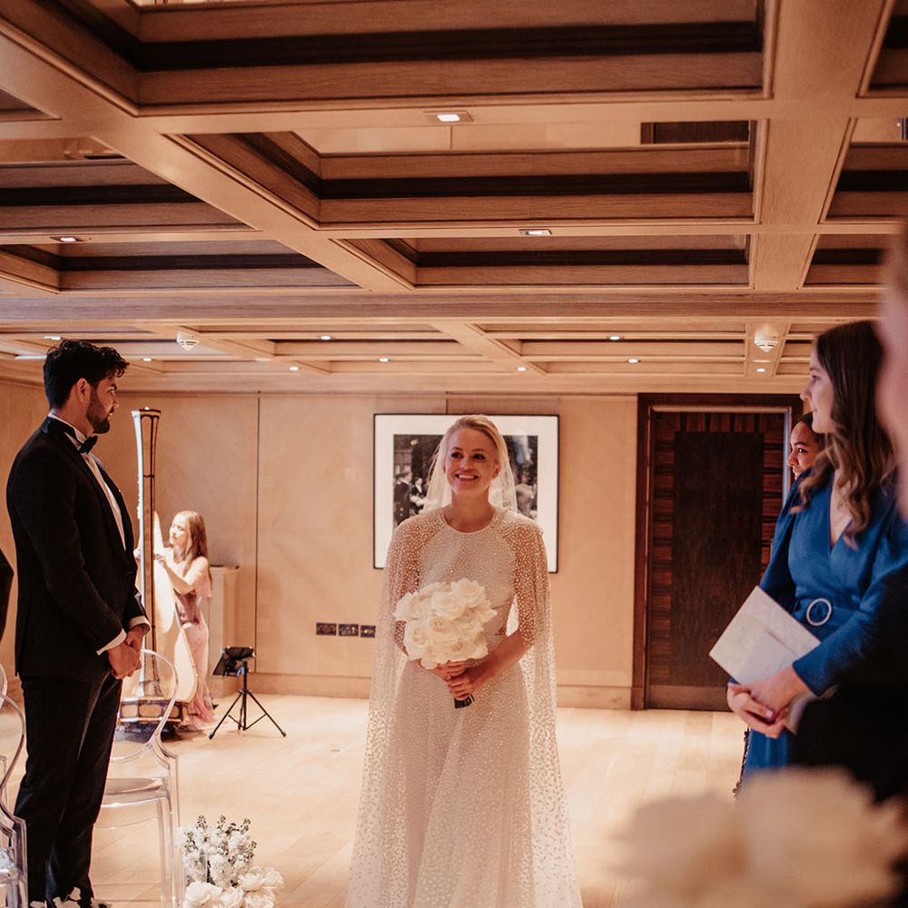 Bride in Jesus Peiro bridal cape with white rose bouquet walks down the aisle 