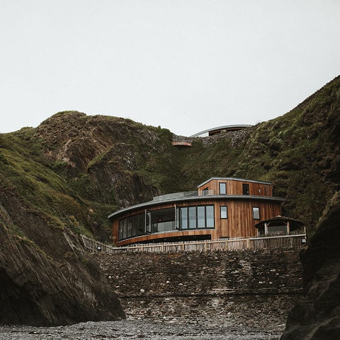 Wooden building with large glass windows sits between rocks at Tunnels Beach