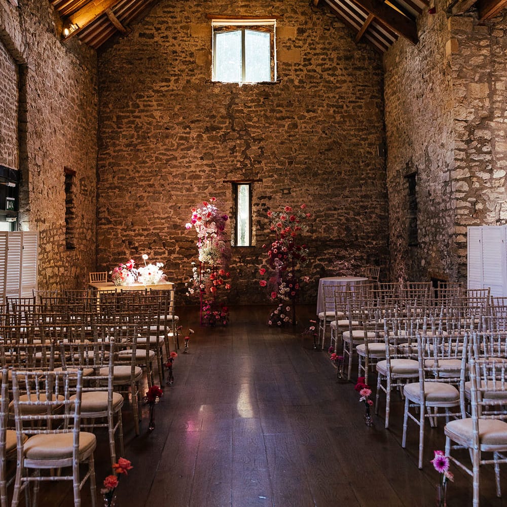 Bright pink floral arch at the end of aisle in front of exposed brick wall with rustic vibe at the Priston Mill wedding venue