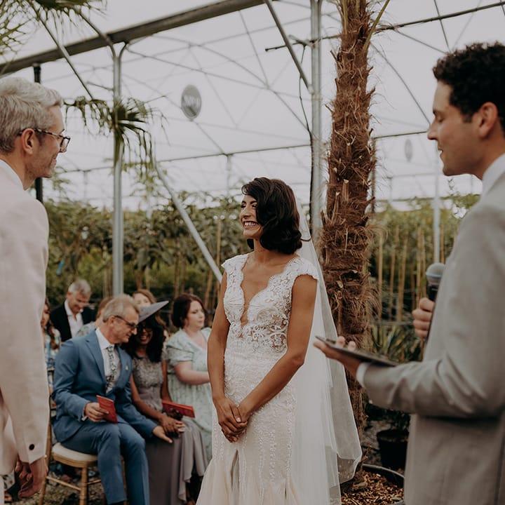 Bride & Groom smile lovingly at each other during ceremony at greenhouse style venue