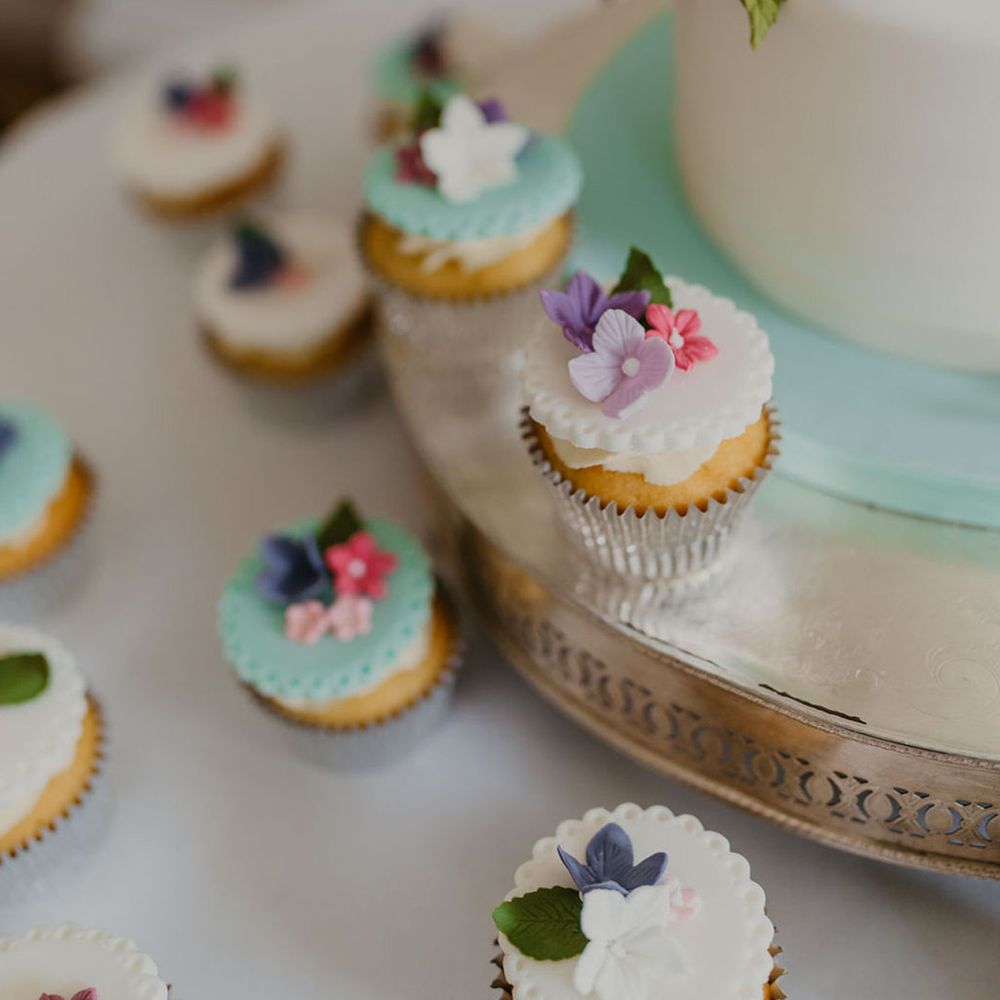 Mini pastel cupcakes surrounded wedding cake finished with floral fondant decor 