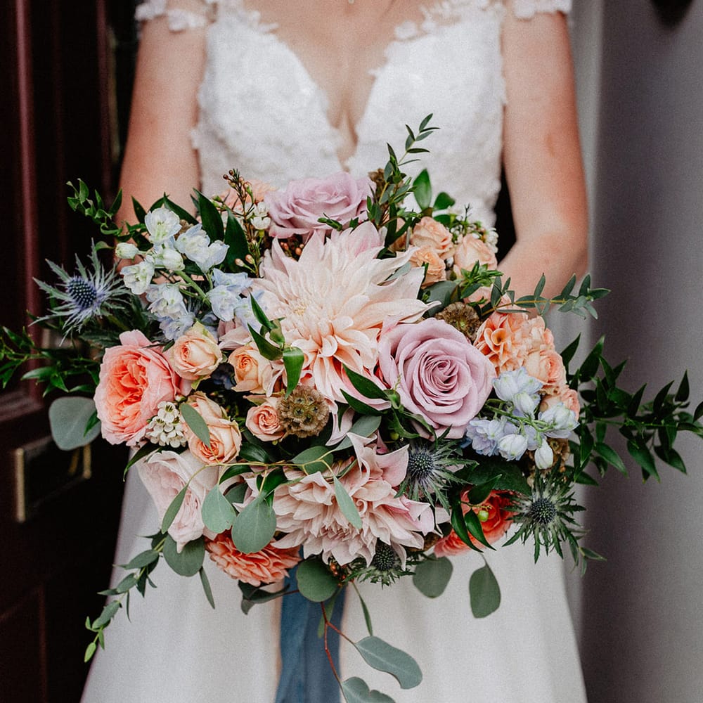 Pink, purple, blue, and peach spring wedding bouquet for the bride with roses and thistle tied with blue ribbon 