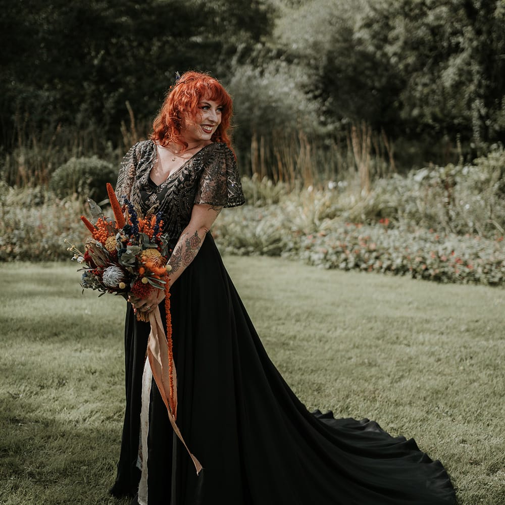 Bride in embellished short sleeve v neck black wedding dress with large burnt orange and eucalyptus dried flower bouquet 