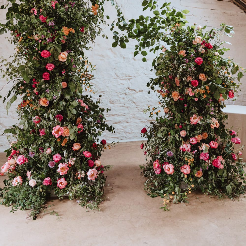 Bright pink rose and peony wedding flower column arrangements decorating the aisle 