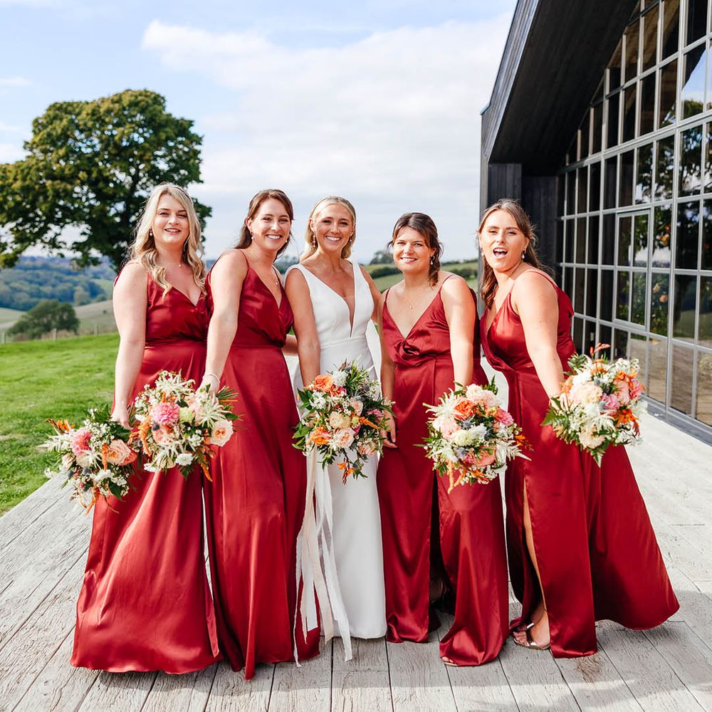 Bridesmaids in red copper satin bridesmaid dresses with the bride in her fitted white wedding dress 