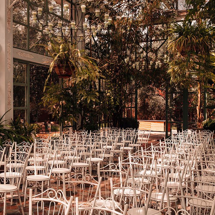 White chairs and botanical plants and foliage decorate the inside of the glass house wedding venue