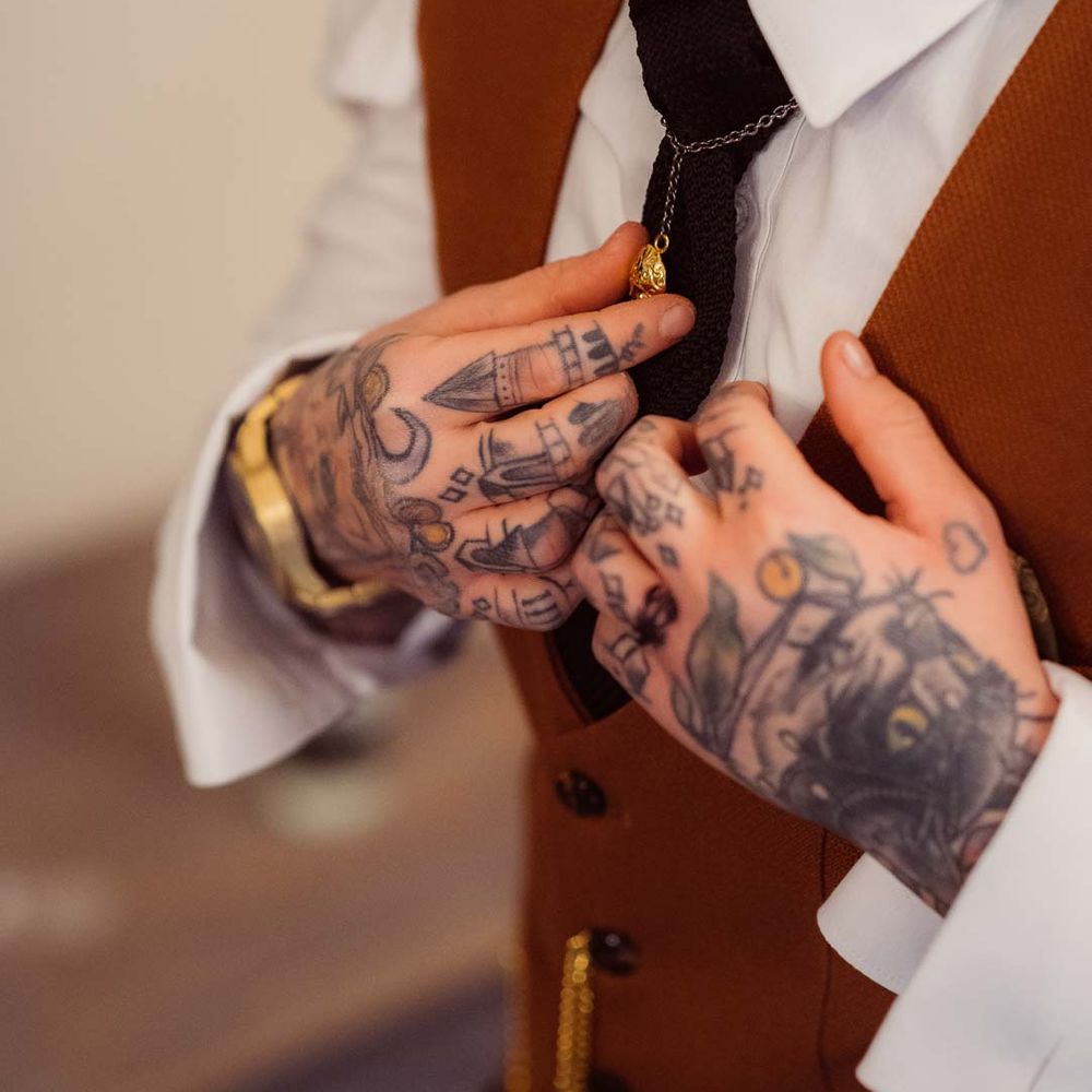 Bride wearing gold watch tying up black tie onto her bridal suit at Kingscote Barn Tetbury 