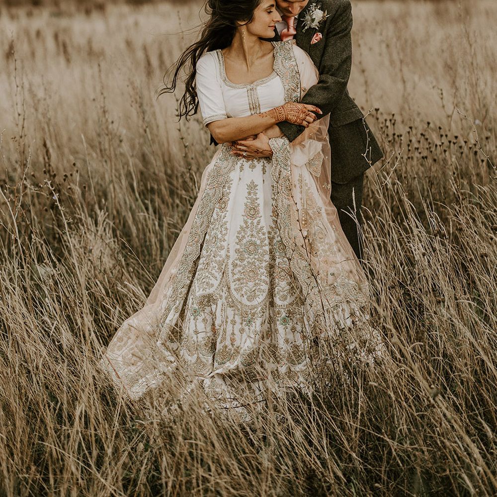 Groom wearing silk pink tie and pocket square embraces the bride from behind for cute couple photo 