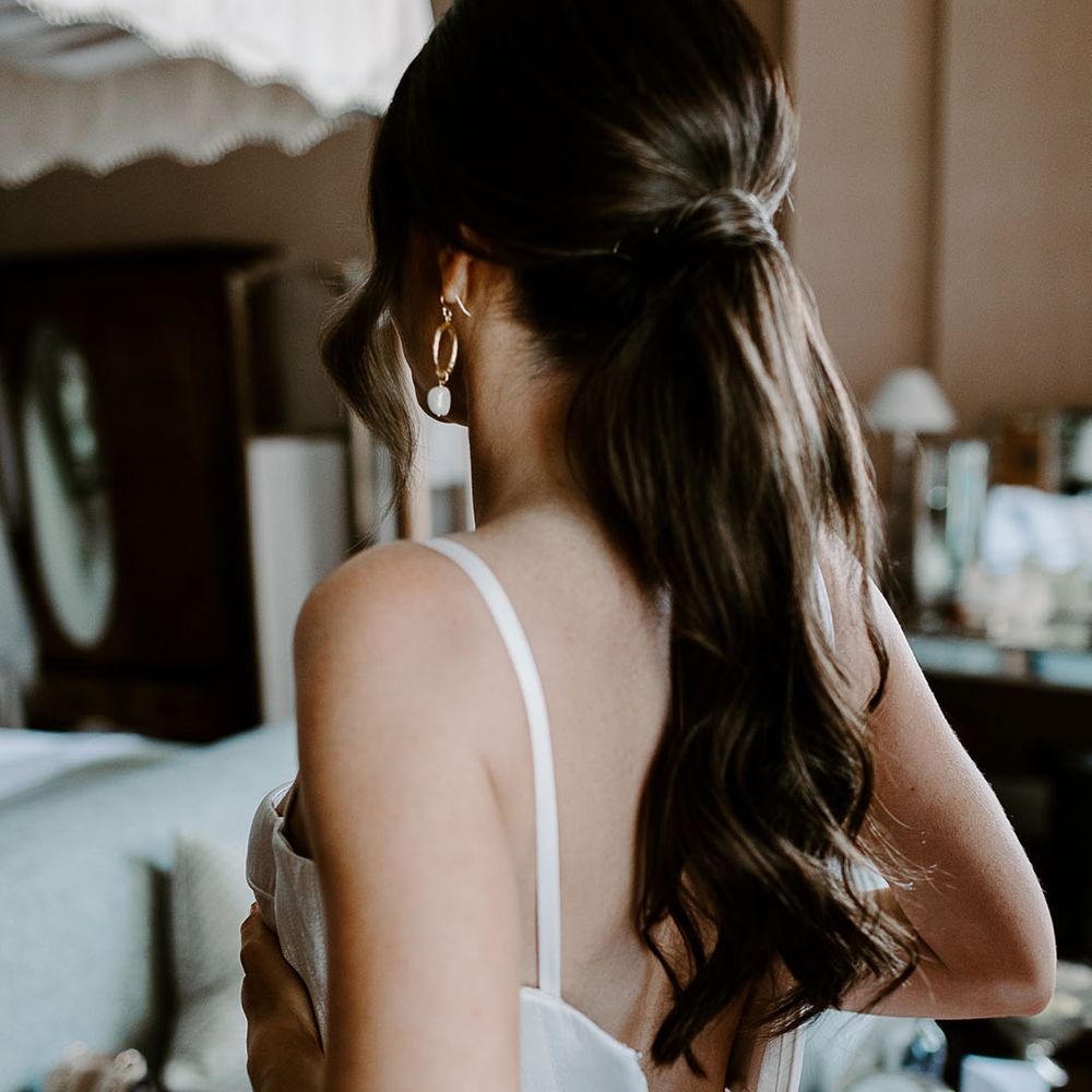 Bride getting into wedding dress wearing her hair in a slick ponytail 