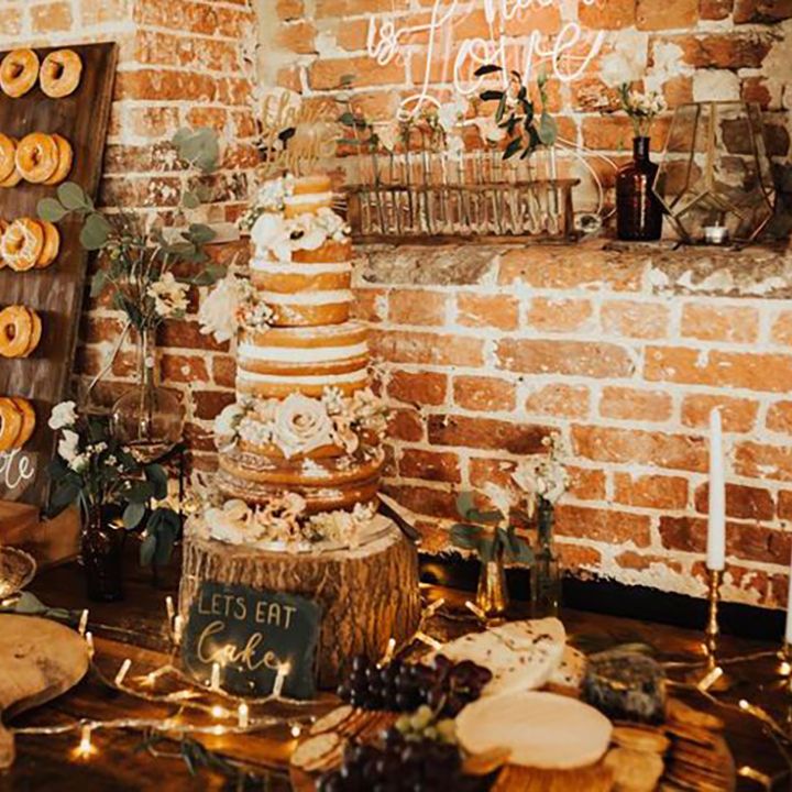 Naked wedding cake at rustic wedding on tree trunk cake stand with dessert table full of doughnuts, cheeses and more 