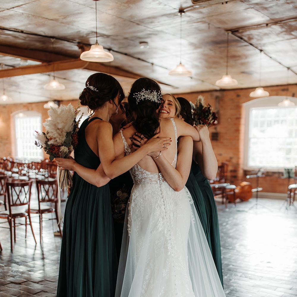 Bridal party in dark green bridesmaid dresses hugging the bride for cute group photo 