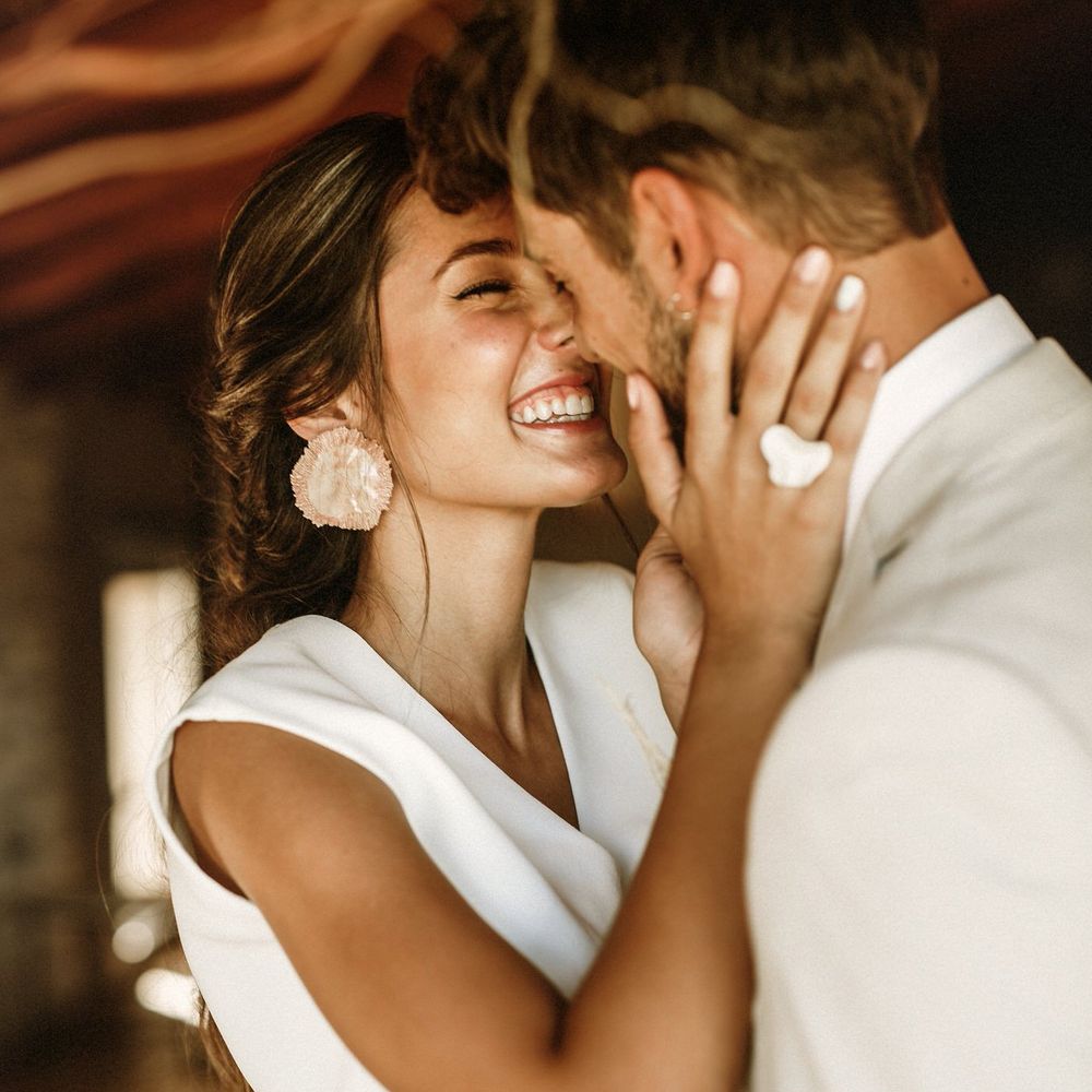 Beautiful bride with natural makeup and strapless bridal top holding her grooms face