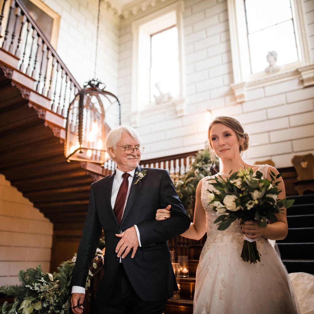 Bride walks down the stairs with her father whilst she holds bouquet