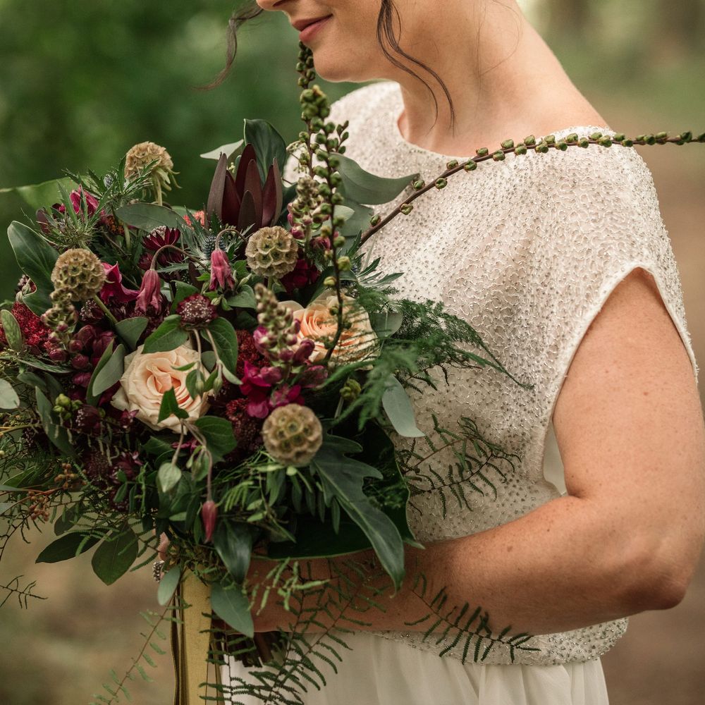 Bride smiles down whilst looking at floral bouquet