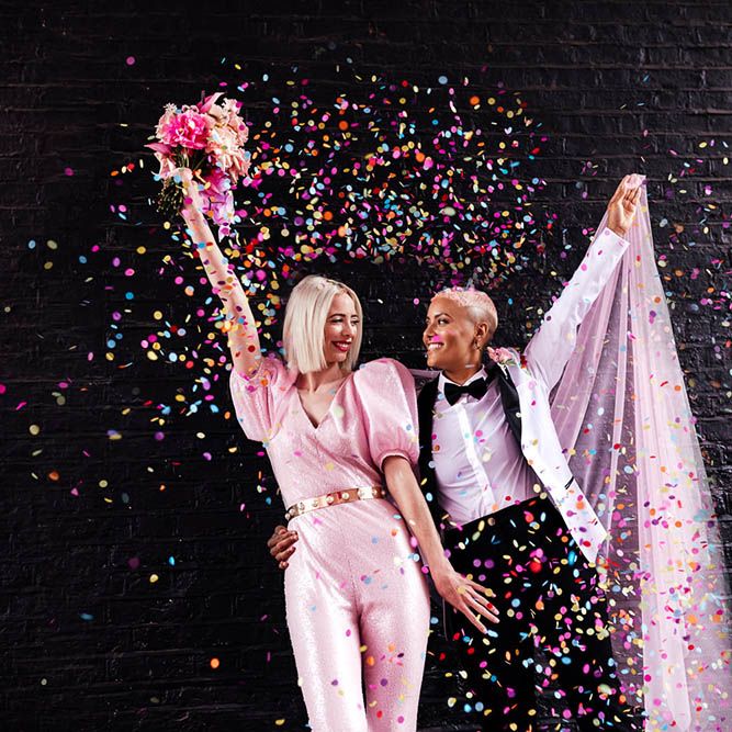 Confetti moment with bride in a fitted pink jumpsuit and white tuxedo jacket 