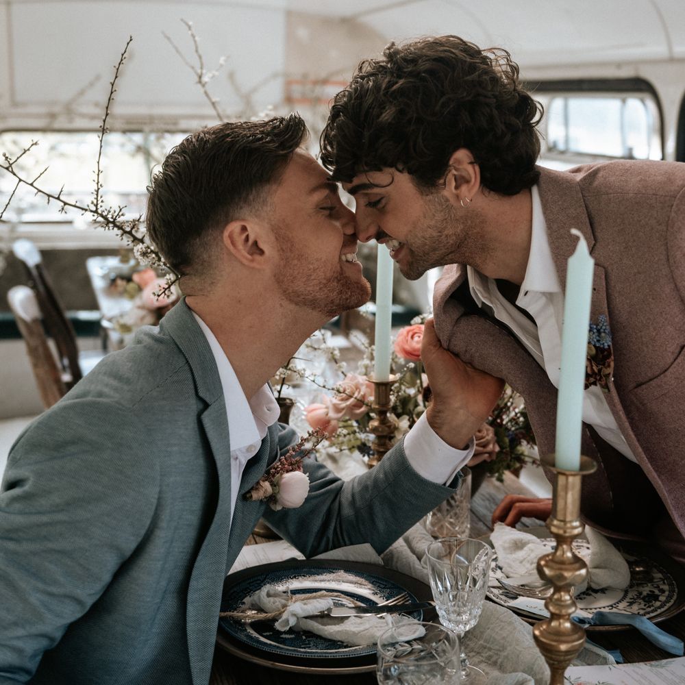 Groom leans across table to kiss groom on their wedding day