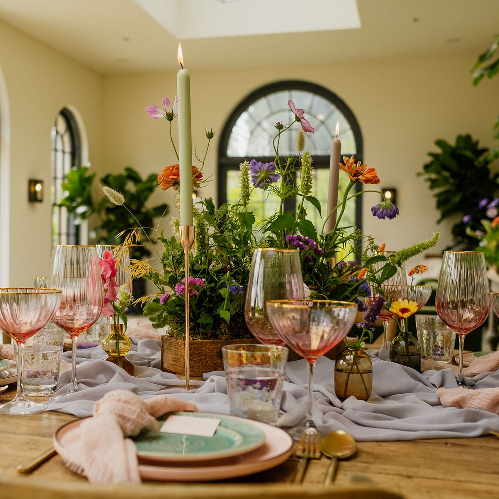 Fiesta theme wedding table decor with wildflower centrepiece decor, taper candles, colourful glassware, linens and ribbon chair back decor 