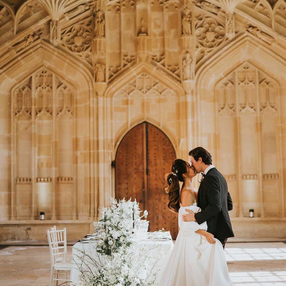 Groom in black tuxedo kissing his bride in a strapless wedding dress with full skirt and detachable sleeves at their monochrome Bodleian wedding 