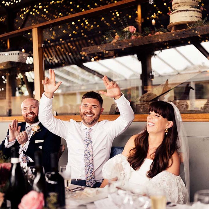 Groom in a floral tie and bride in a strapless wedding dress with lace puff sleeves laughing at the top table 