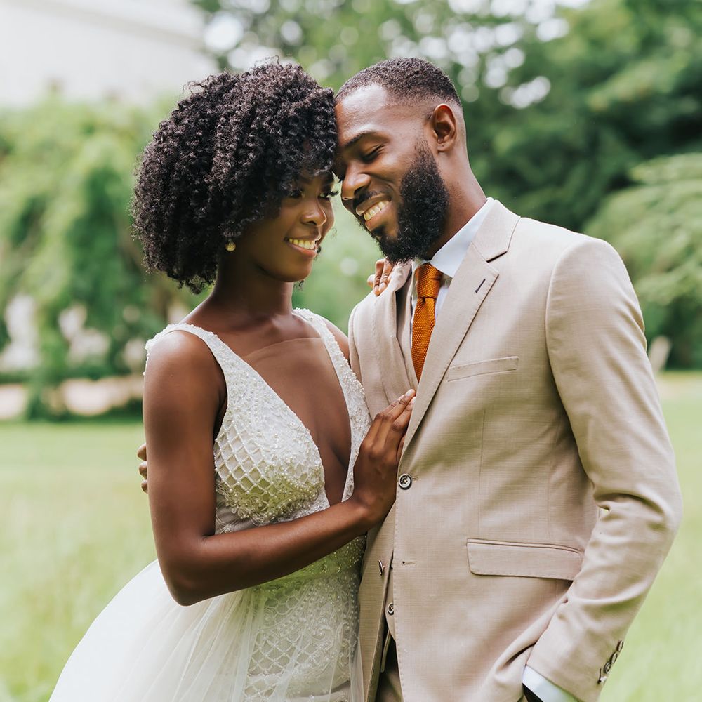 Intimate bride and groom portrait with groom in a beige suit and bride with afro hair in a plunging neckline wedding dress with embellished detail