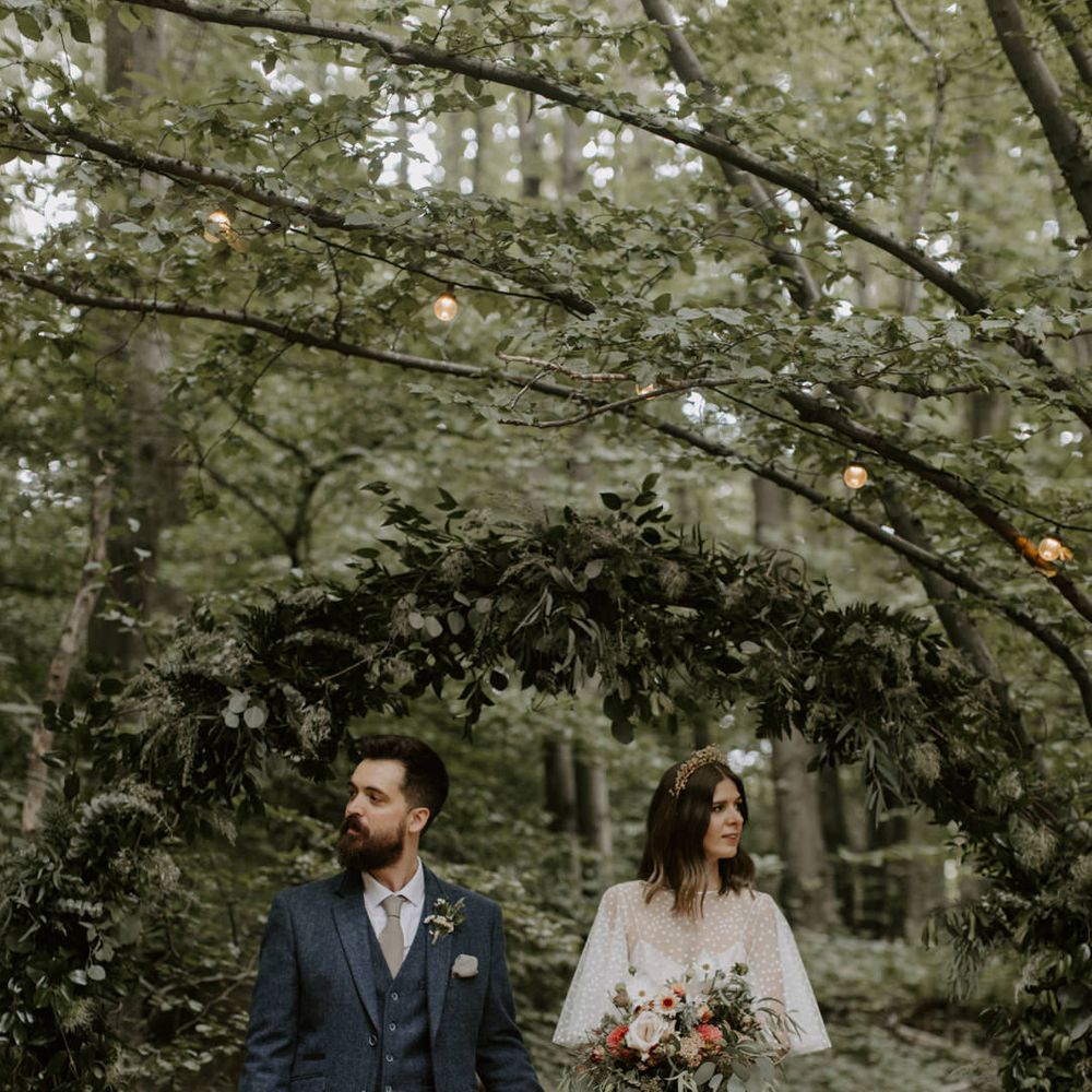 Bride & groom walk under archway covered in green foliage