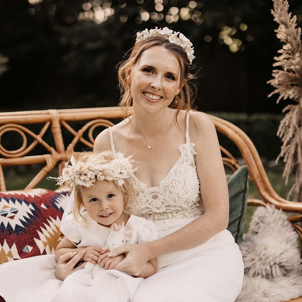 Bride sits with her daughter outdoors who wears dried floral crown