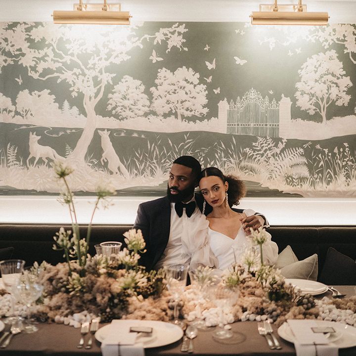 Black bride and groom sitting at their stylish wedding reception at Mayfair Townhouse with green and white flowers 