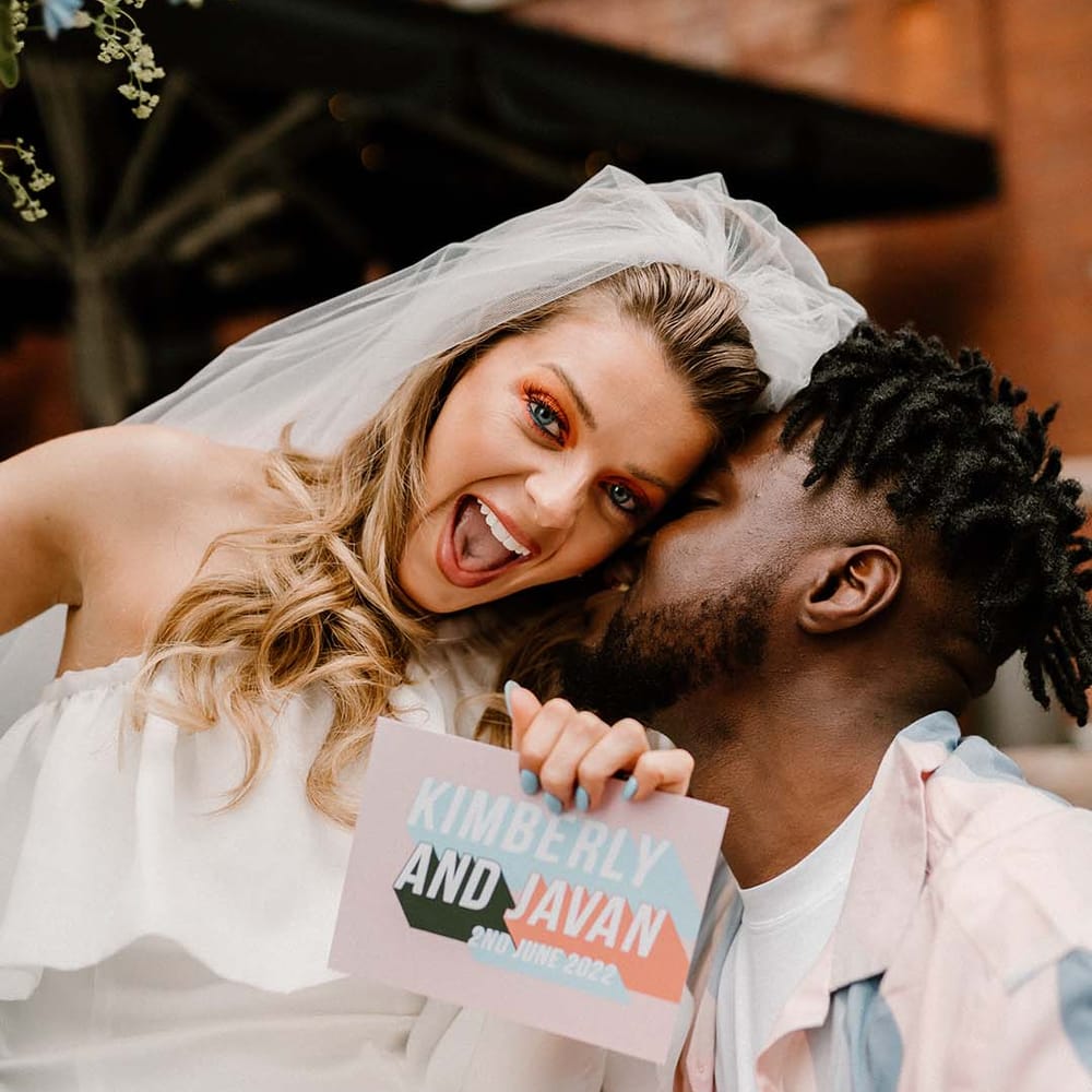 Bride in a short off the shoulder wedding dress holding a contemporary pastel wedding invitation