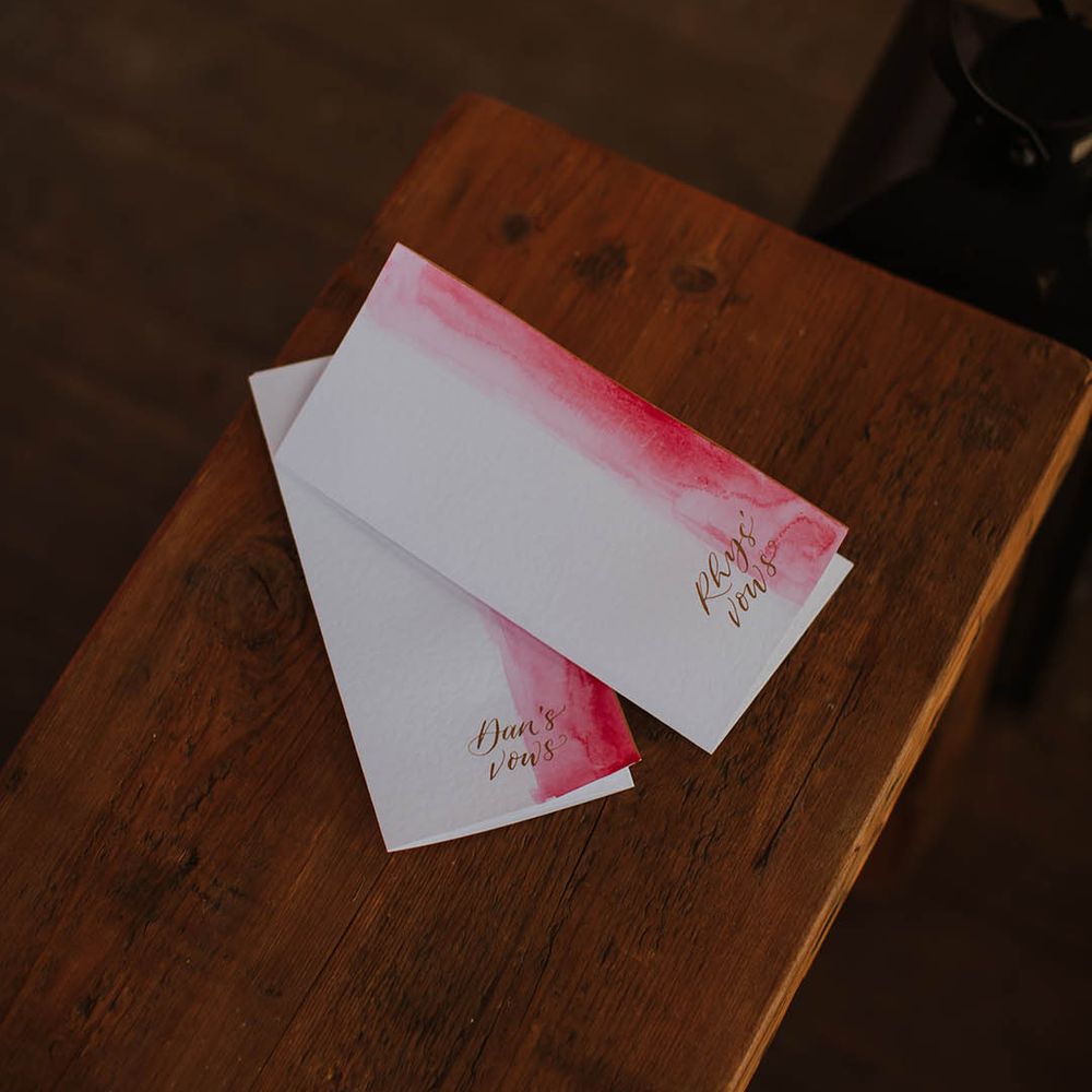 Pink and white vow booklets on wooden bench 