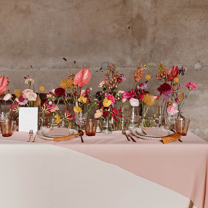 Intimate wedding reception table decor with pink and yellow flower stems in bottles 
