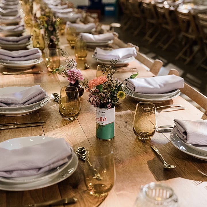 White plates with lilac napkins and coloured glassware for table setting decorations with tin can vases of flowers