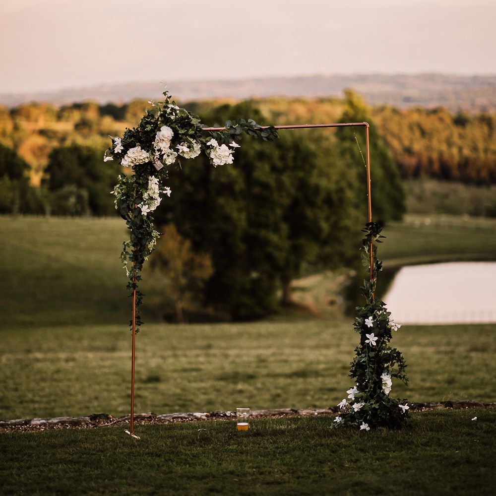 Copper frame decorated with foliage and white flowers in the gardens of Wadhurst Castle wedding venue 