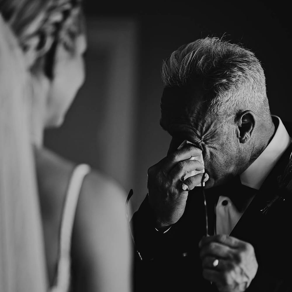 Father of the bride wipes his eyes as he sees the bride 